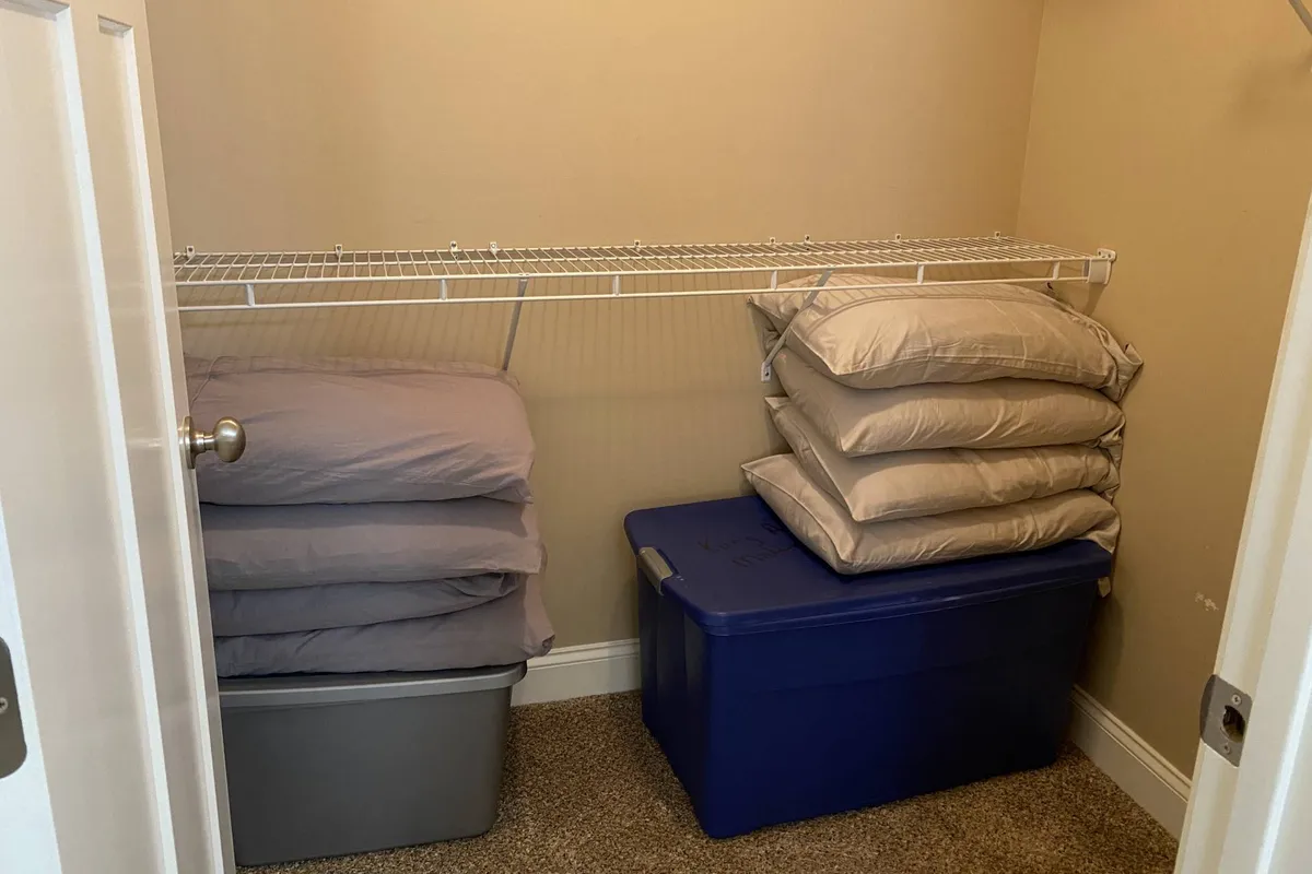 Shelving with neatly organized bedding and storage bins, showcasing practical storage options and thoughtful use of space near the entrance or garage area.