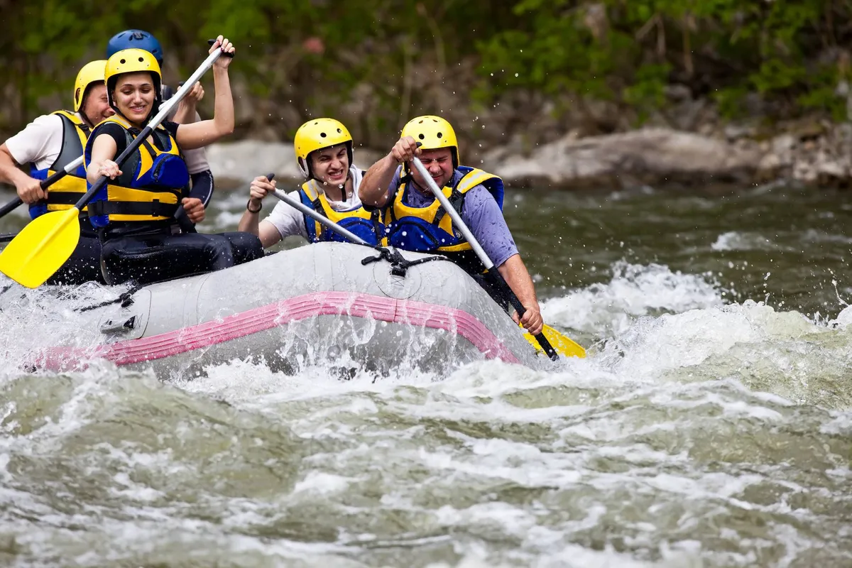 A raft filled with participants navigates lively white-water rapids, each person engaged with paddles as water splashes around. The scene is packed with energy and teamwork, capturing the thrill of adventure sports on the river.