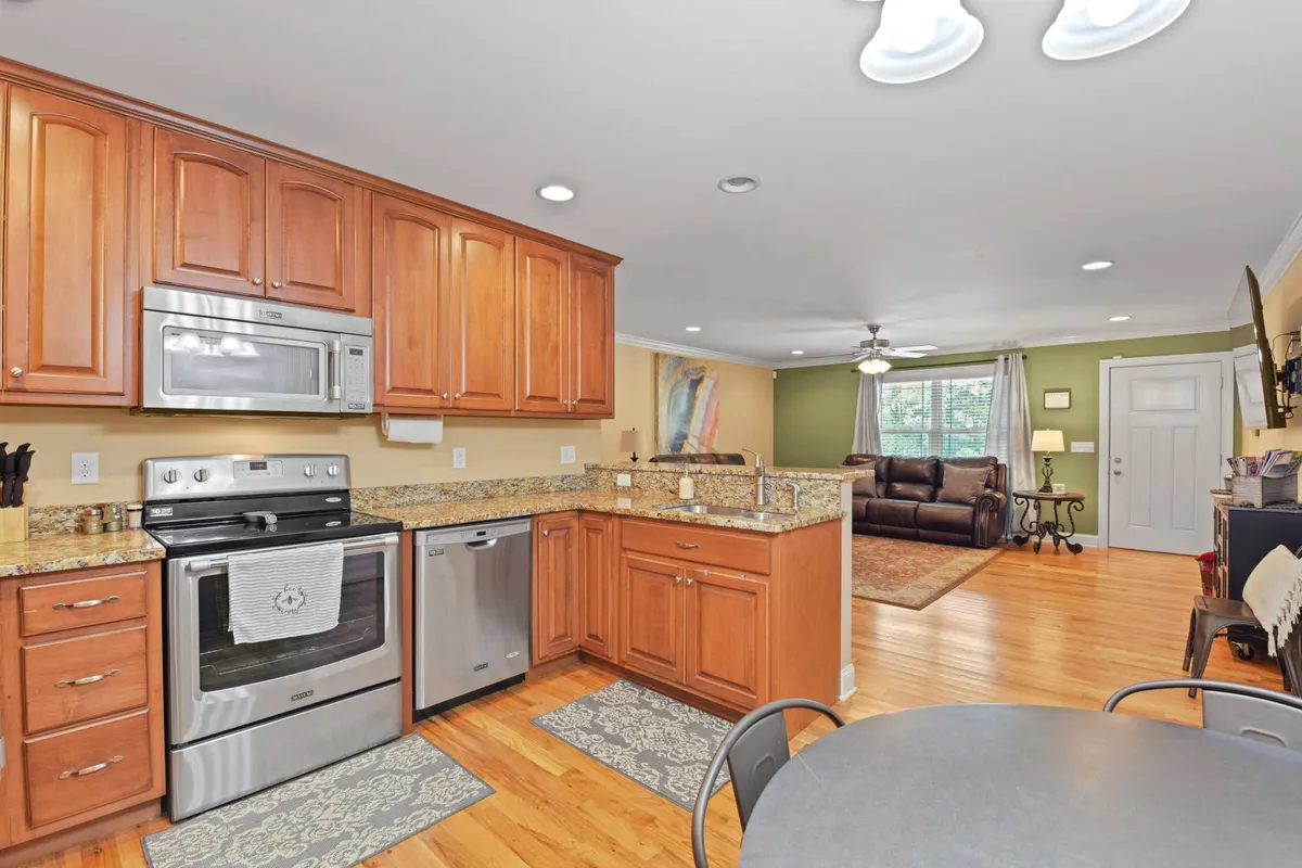 A spacious, open-concept kitchen with striking granite countertops and stainless steel appliances. The image features wood cabinets, a dining table set for a meal, and a glimpse of the adjoining living area, suggesting seamless flow for gatherings. The countertops are uncluttered, highlighting a well-organized and inviting cooking space.