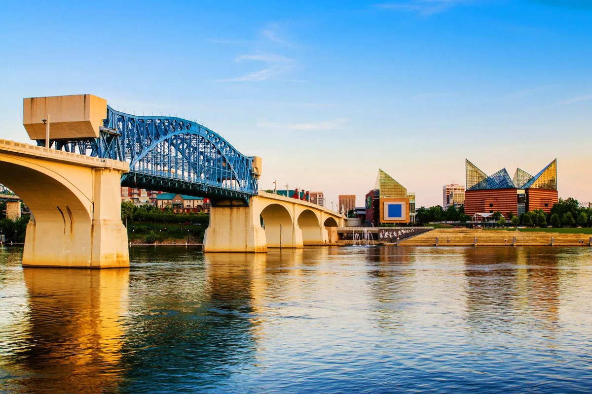 A scenic view of a blue bridge spanning reflective water, modern buildings, and serene surroundings. The setting sun casts a soft glow, and the scene invites exploration, photography, and leisurely walks along the waterfront.