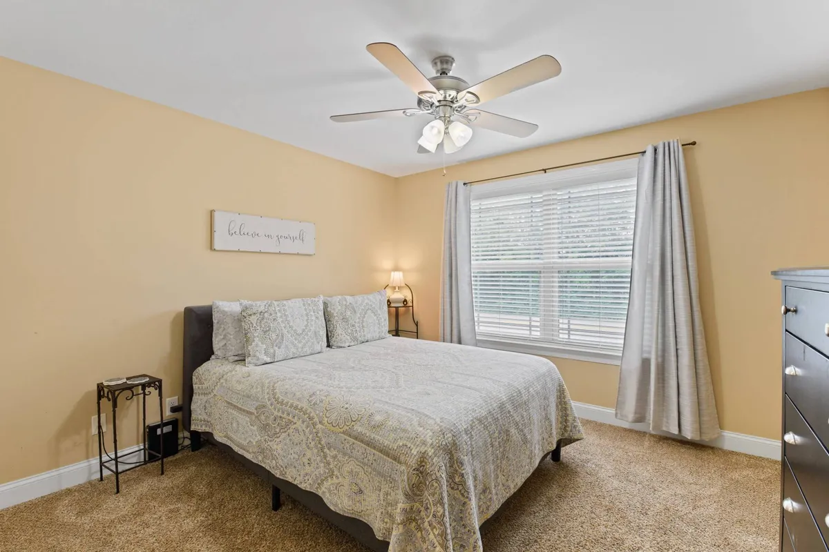 A charming second bedroom with a queen-size bed dressed in patterned bedding, a window framed by curtains, and wall décor featuring a motivational quote. The space exudes calm and offers another private, comfortable sleeping area.