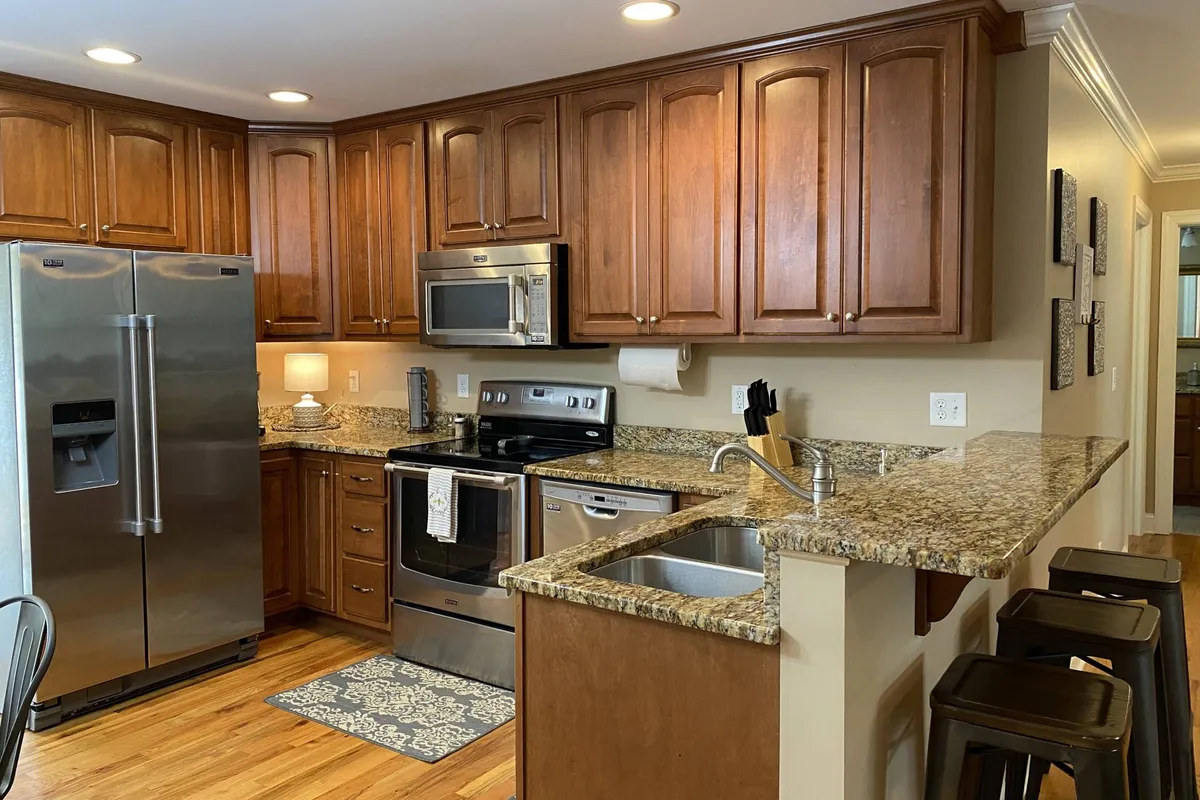 A welcoming kitchen scene with gleaming stainless steel appliances, granite countertops, and bar stools tucked under the counter. Warm wood cabinetry adds a homey touch. The space is ready for anything from morning coffee to celebratory dinners, with all essentials at hand.