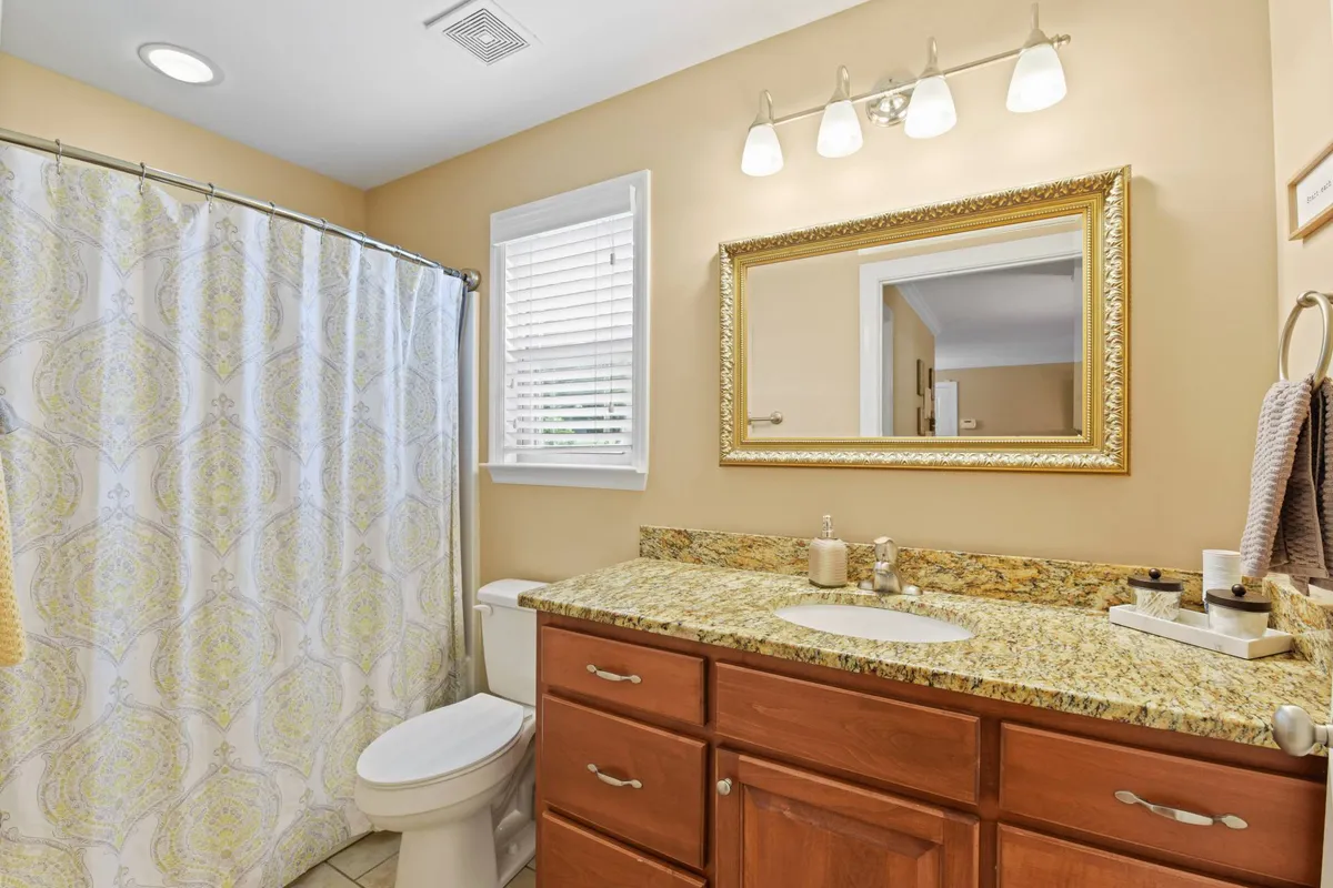 A well-appointed bathroom with a granite countertop, large mirror, and shower curtain, bathed in soft morning sunlight. The space is ideal for personal grooming and relaxation, with an ambiance that suggests cleanliness and care.