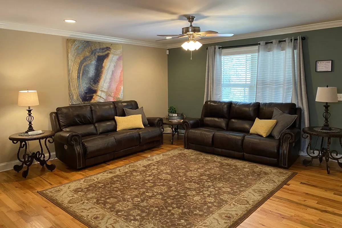 This image captures a cozy living room with plush brown leather sofas arranged around a decorative rug, complemented by wall art and warm lighting from lamps. The setup invites relaxation and socializing, making it an ideal spot for gatherings, movie nights, or quiet family moments.